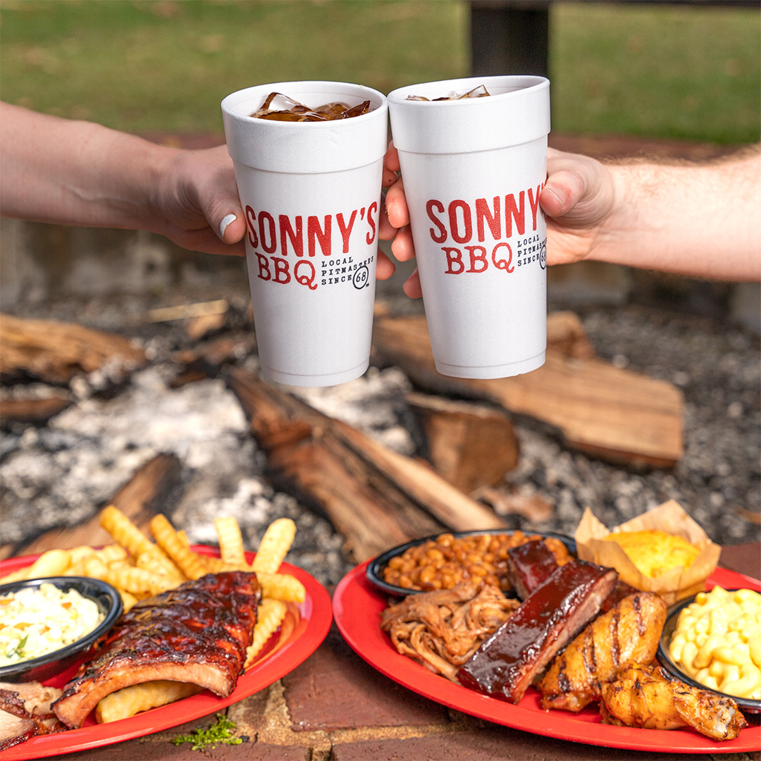 Two people cheers Sweet Tea above two Pick of the Pit Combos. Both 2 and 3-meat options are pictured with various sidekicks and bread.