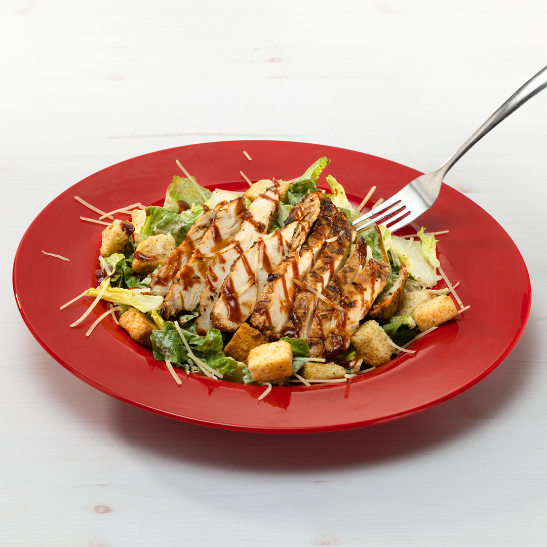 Romaine lettuce in bowl, topped with croutons, grilled chicken, Smokin' BBQ Sauce and Caesar Dressing