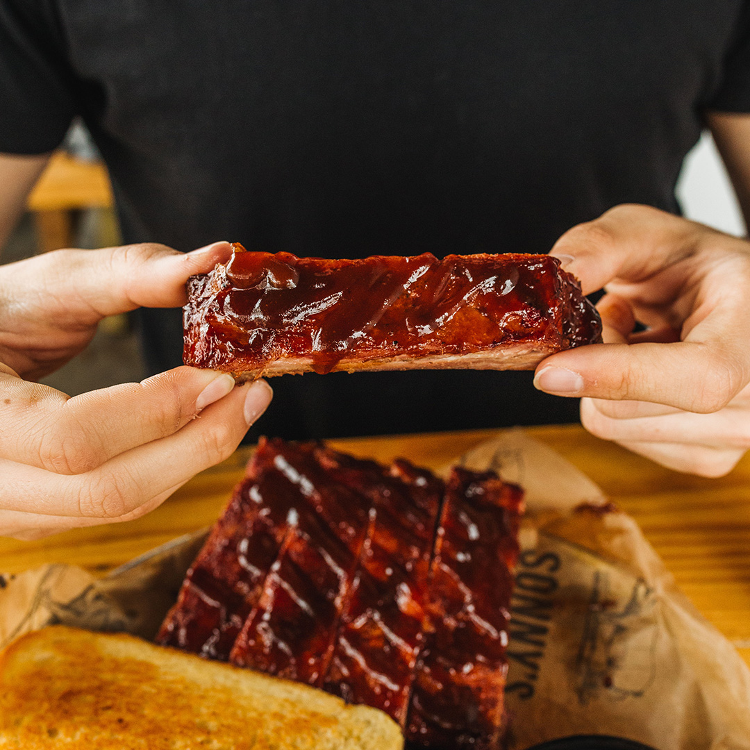 Guest holds up Sweet and Smokey St. Louis Rib above plate.